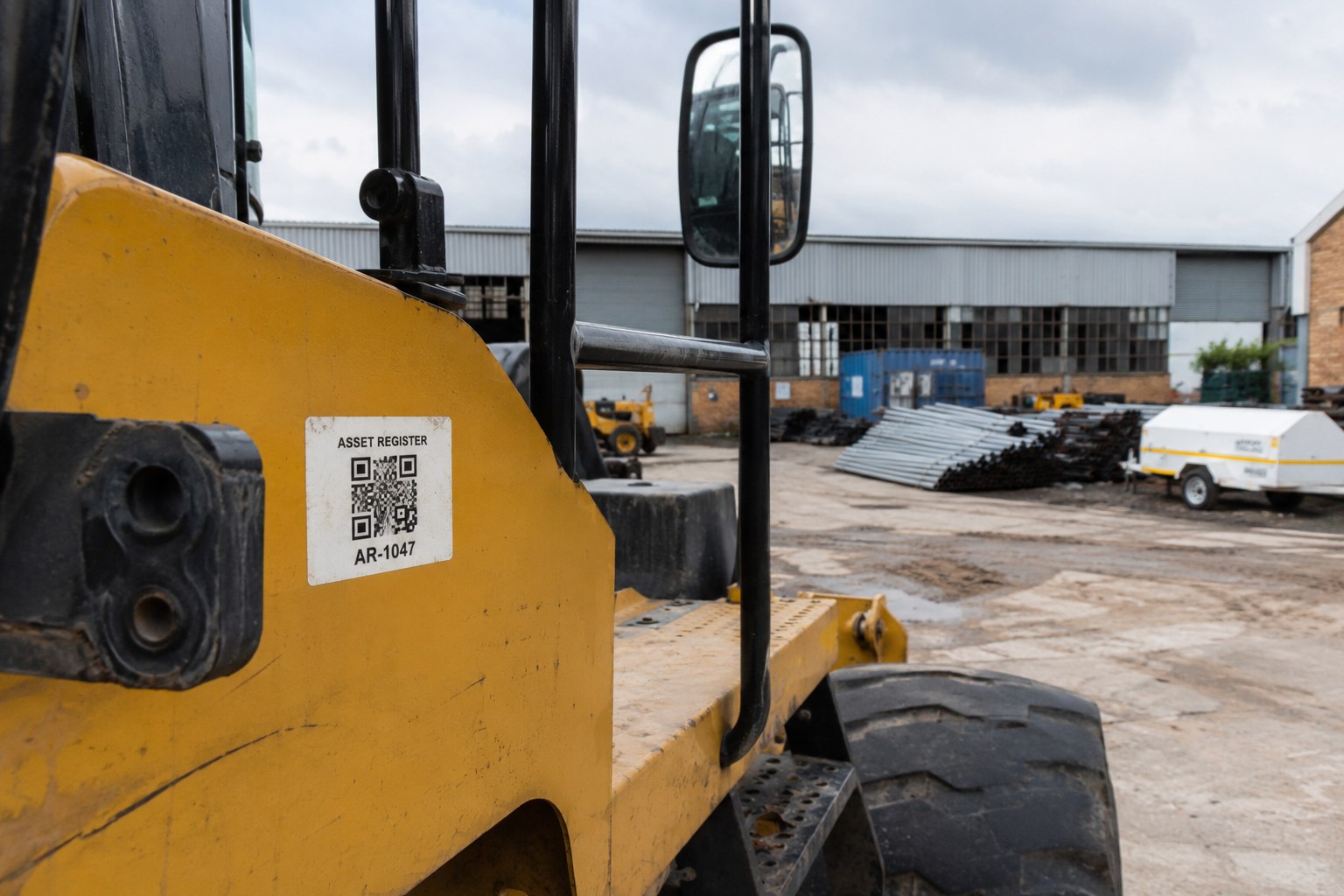 A QR-coded asset register tag on a piece of heavy yellow equipment in a yard